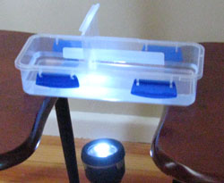 A plastic container between two chairs with a torch shining up beneath the container.
