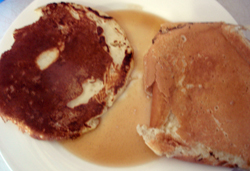 Two pancakes and maple syrup on a plate.