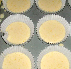 Six patty pan paper liners in a patty pan. They are each about half full of batter.