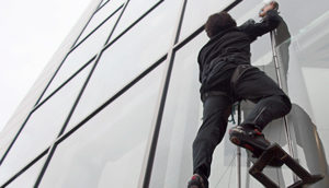 A person wearing gloves and a harness climbing stright up a glass wall.