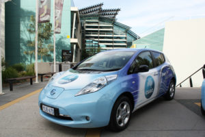 An electric car outside a big building.