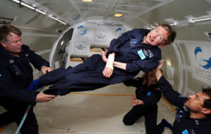 Photograph of Stephen Hawkings floating in a capsule with three people assisting him.