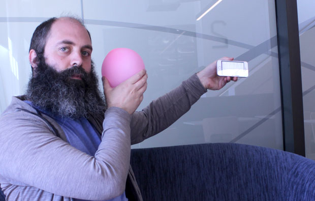 A man holdiing a pink baloon near his face and a phone at arms length.