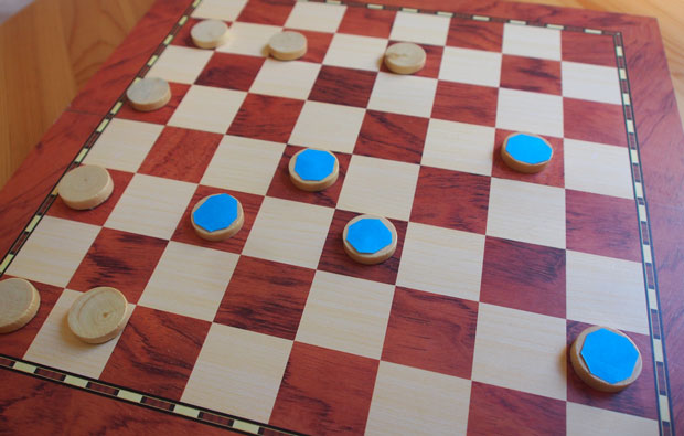 Image of a chess board with some blue and some white tokens.