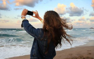 Girl taking a photo of the clouds at the beach