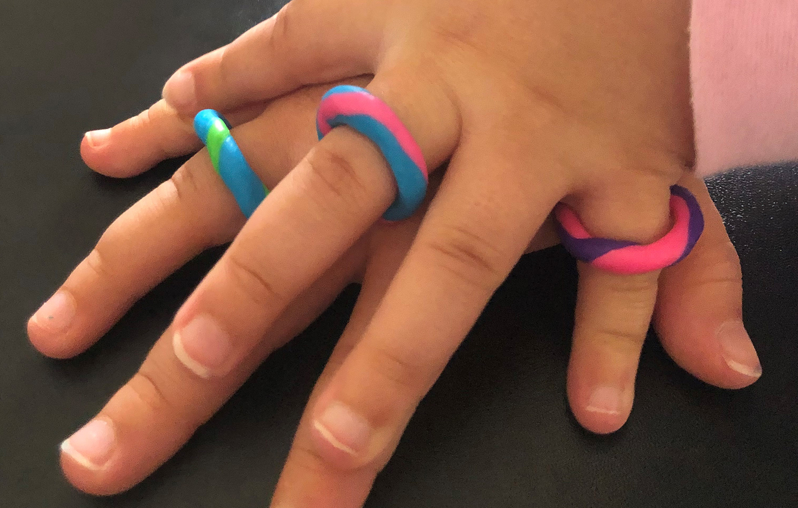 A child's hand ontop of a larger hand, both hands are wearing colourful rings