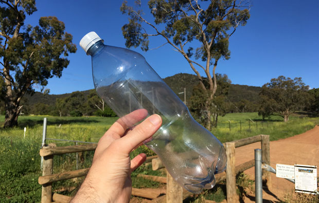 Holding up an empty drink bottle with mountain in the background.