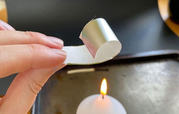 Foil and paper strip curling as it is held over a candle flame.