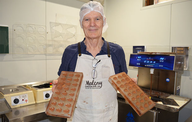 A man in an apron and hairnet, holding two chocolate trays