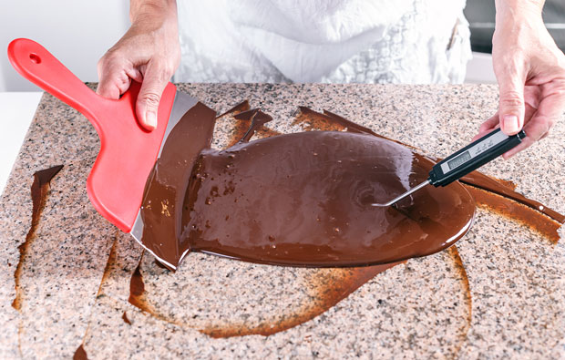 Someone working with melted chocolate, using a scraper and a thermometer
