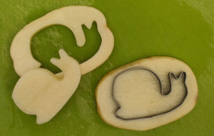 Snail shaped cookie cutter cutting out 2 slices from a potato.