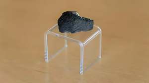 A dark rock sitting on a Perspex stand.
